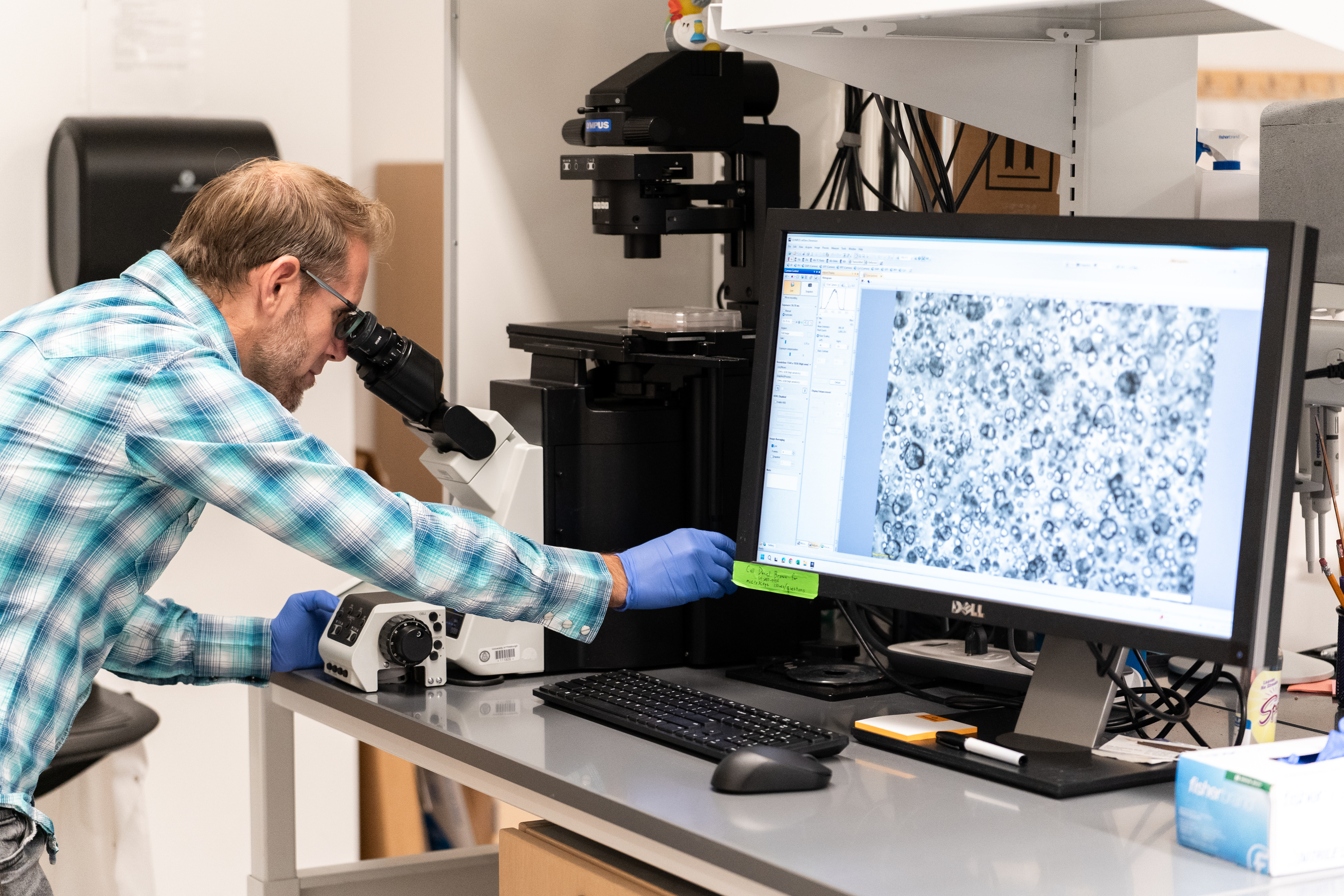 Person looking through a microscope with a computer displaying microscope image.